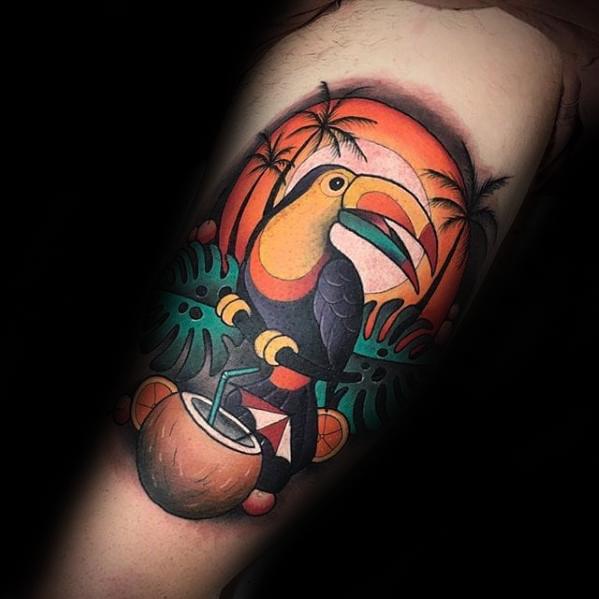 Vibrant toucan tattoo with a tropical sunset, palm trees, and coconut drink, creating a bold beach-themed scene on the upper arm.