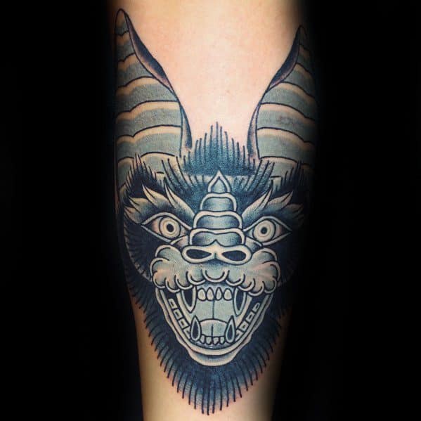 Bold traditional bat tattoo with a mythical, dragon-like face, striped horns, sharp teeth, and intense black and grey shading.