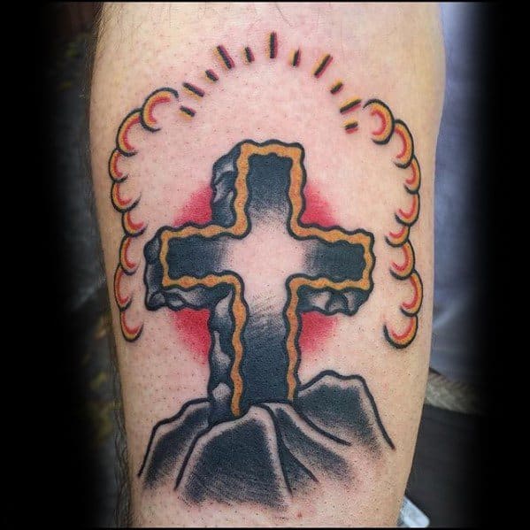 Traditional-style tattoo of a glowing stone cross on a mountain with red shading and curved rays of light surrounding the top.