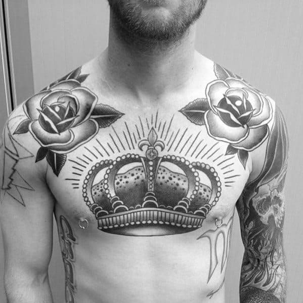 Chest tattoo featuring a detailed crown at the center with shaded rays and bold roses on each shoulder in classic black and grey style.