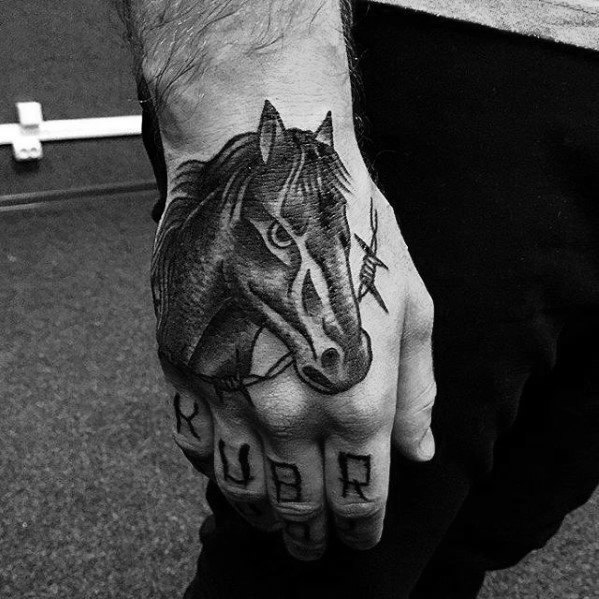 Black and grey horse head tattoo on the hand with bold shading, barbed wire detail, and lettering across the fingers.