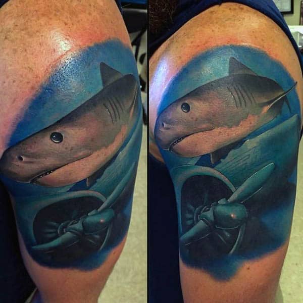 Tattoo of a shark swimming among the wreckage of an underwater airplane on an upper arm