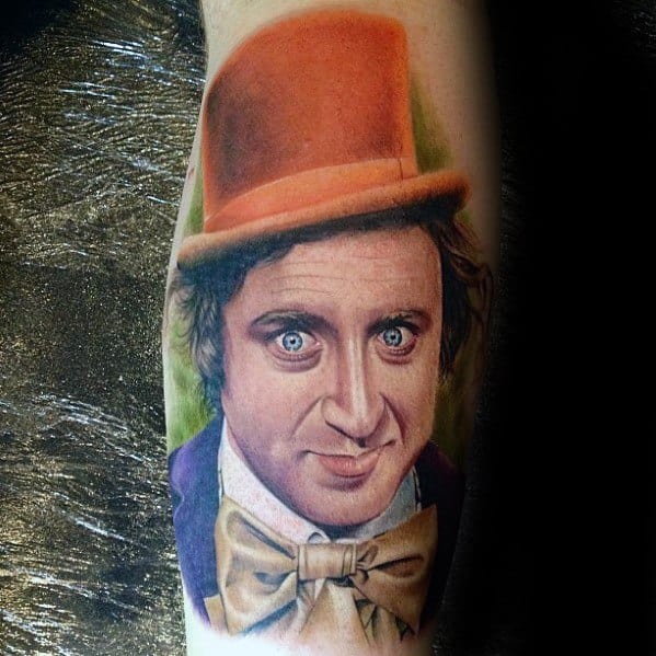 Vibrant Willy Wonka tattoo with piercing blue eyes, orange top hat, and cream bow tie, capturing a mischievous expression.