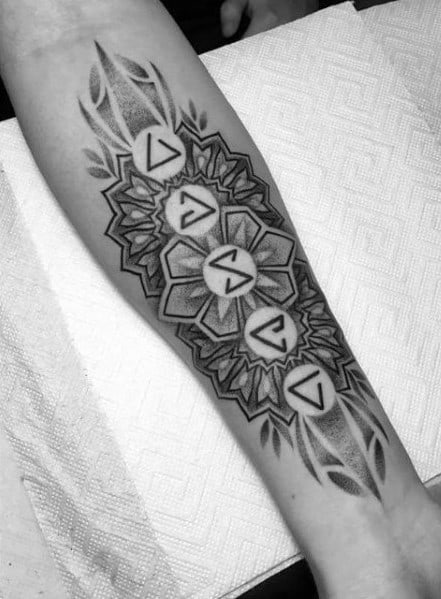 Intricate Witcher forearm tattoo with magical signs set inside a bold mandala pattern and accented by leaf-like shapes.
