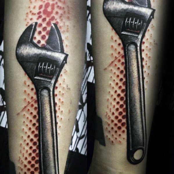 Realistic tattoo of a metallic adjustable wrench over red textured skin, creating a 3D embedded effect on the forearm.