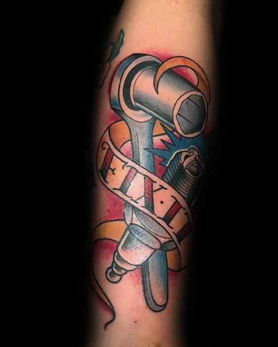 Tattoo of a wrench and spark plug wrapped in a ribbon that reads FIX IT, with bold colors and a comic-style blue burst background.