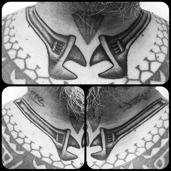 Black and grey chest tattoo of two large wrenches mirrored at the collarbone, blending into tribal-style patterns.