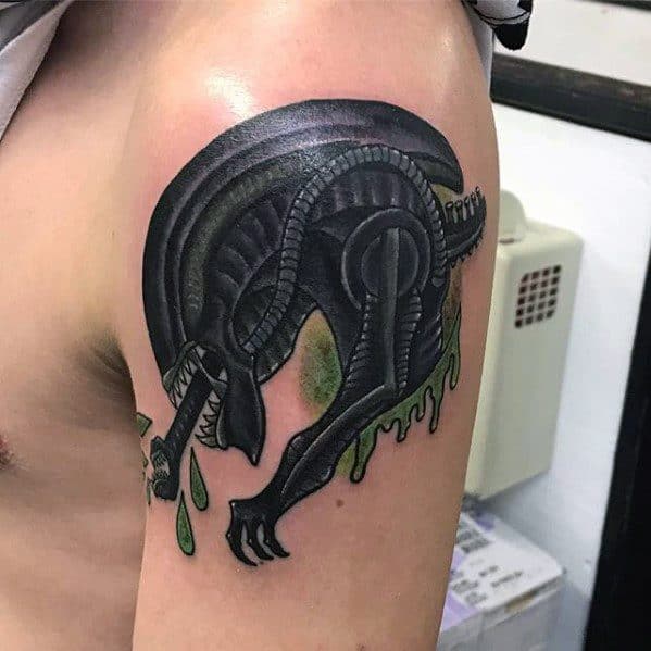 Bold black Xenomorph tattoo on upper arm with cartoonish style, green slime dripping from claws and mouth.