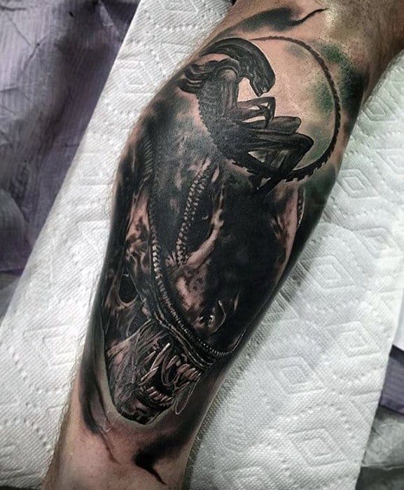 Dark and detailed Xenomorph tattoo on leg showing both a frontal view of the snarling face and a crouching silhouette above.