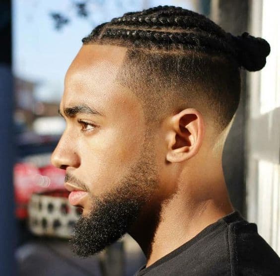 A black man wearing twists secured together on top to form a man bun