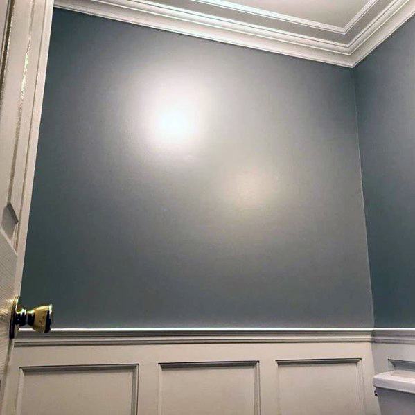 A half-bath featuring soft blue walls with white crown molding and wainscoting, creating a clean and elegant look