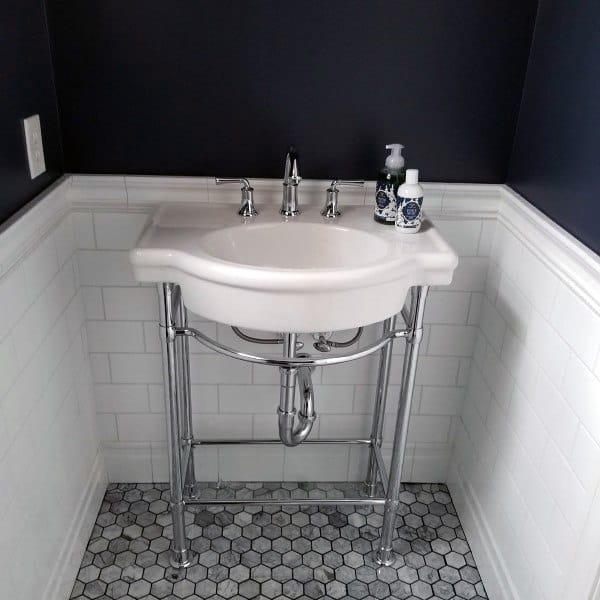 Half bath with a small white corner sink, chrome legs, dark walls, and hexagonal tile floor, soap bottles on the sink