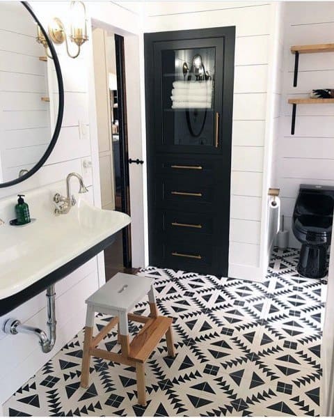 Modern farmhouse bathroom with black cabinet, geometric tile floor, wall sink, and shelves.