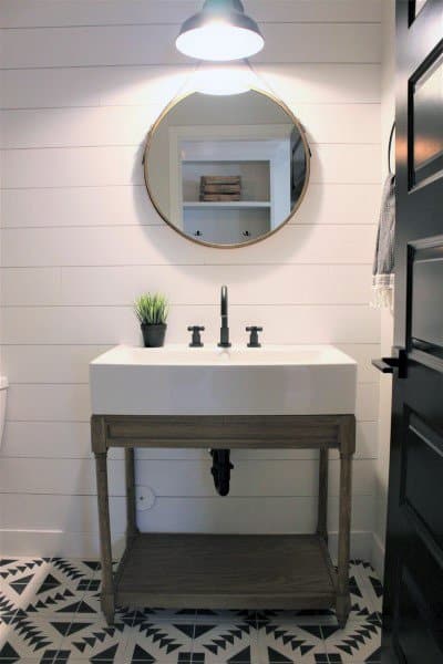 A modern half bath with a round mirror, white sink, and black fixtures on a geometric patterned floor