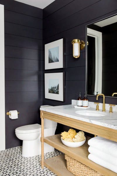 Half bath with black shiplap walls, wooden vanity, gold fixtures, and framed art decor