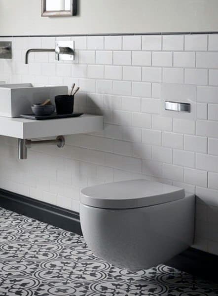 A modern half bath with a wall-mounted toilet, white subway tiles, a sink, and patterned floor tiles