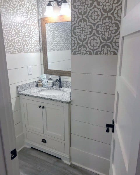 Small white bathroom with gray patterned wallpaper, wood-framed mirror, and shiplap walls.
