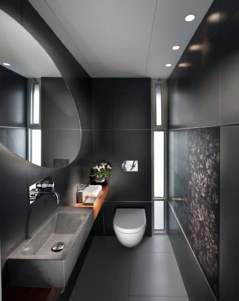 Modern half bath with dark walls, oval mirror, sleek vanity, and white toilet under recessed lighting