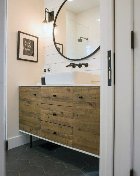 Rustic bathroom featuring a round mirror, wooden vanity, and wall-mounted light fixture