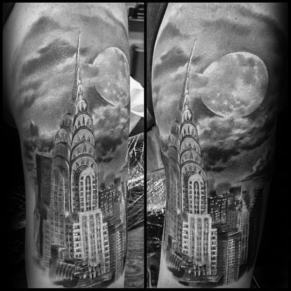 Realistic black and gray upper arm tattoo of the Chrysler Building with a full moon and dramatic clouds in the night sky.