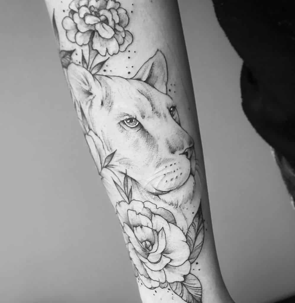 Delicate black and grey lioness tattoo on the forearm, featuring soft shading, floral details, and fine dotwork for a graceful, feminine design.