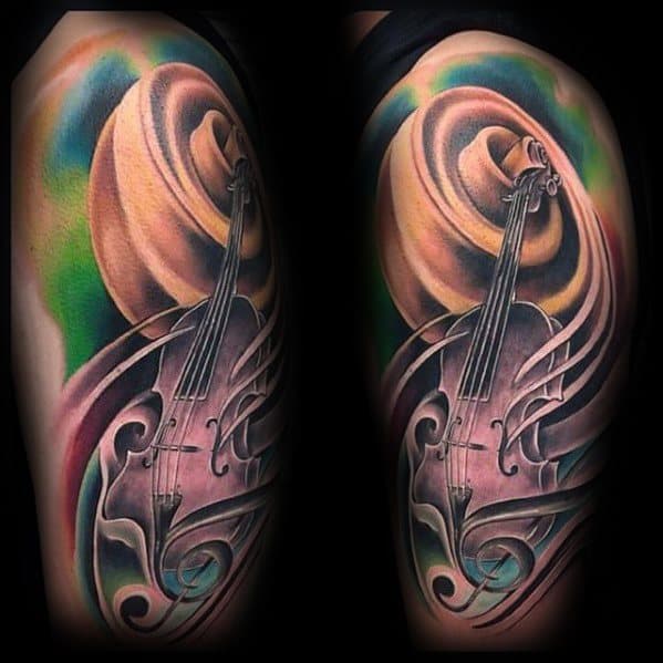 Vibrant upper arm tattoo of a violin with swirling abstract shapes and a large cowboy hat, blending musical and Western themes in bold colors.