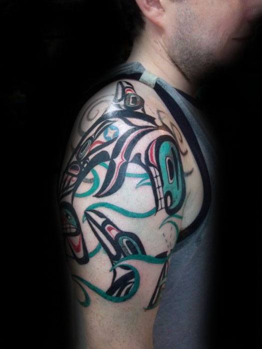 Vivid and dynamic orca tattoo on the upper arm, featuring a tribal-inspired design with flowing lines, bold shapes, and vibrant colors, capturing movement and energy.