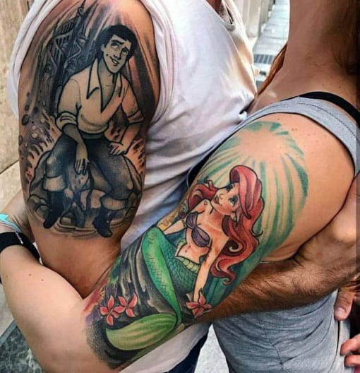 Matching upper arm tattoos of Prince Eric and Ariel from *The Little Mermaid*, symbolizing a magical and timeless love story.