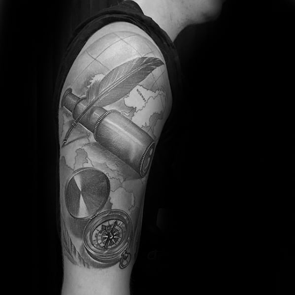 Tattoo of a feather, compass, and inkwell on an upper arm with a telescope and map background