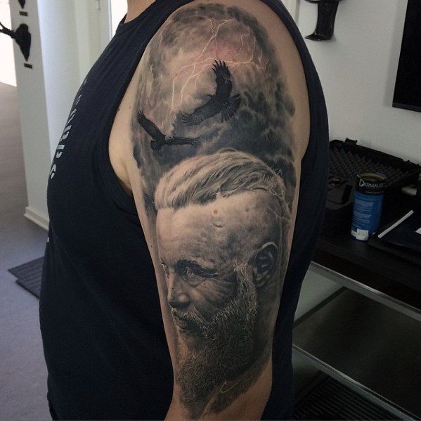 A detailed arm tattoo featuring a bearded man with ravens and lightning in the background