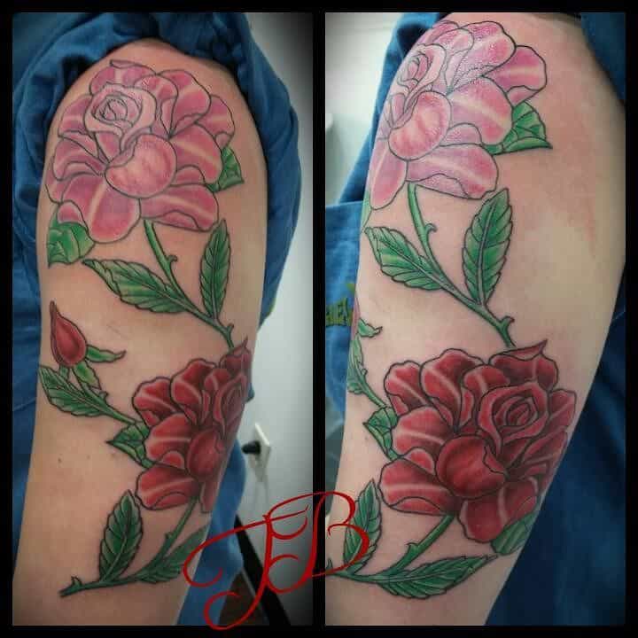 A stunning half sleeve tattoo featuring pink and red roses intertwined with lush green leaves graces the person's arm