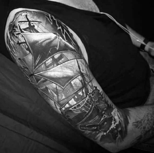 Detailed black-and-gray tattoo of a stormy sailing ship, complete with crashing waves and bottle that appears from the ocean