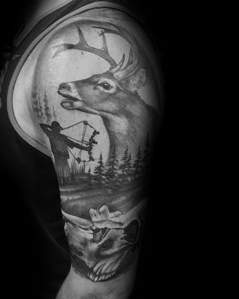 Realistic black and grey upper arm tattoo of a buck in the forest with a bowhunter silhouette below and a deer skull at the bottom.