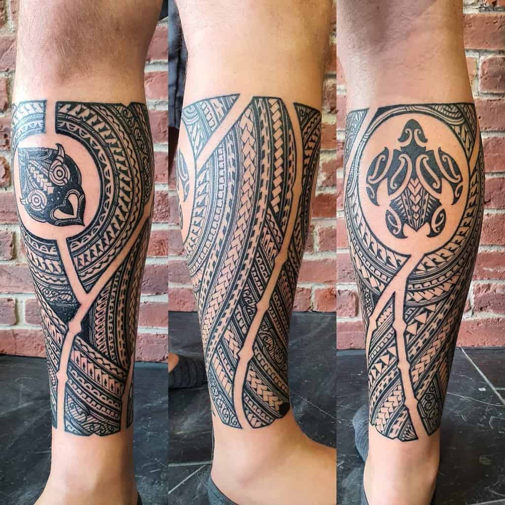 Intricate black and grey tribal tattoo, featuring geometric patterns, a turtle and Tiki mask motif, and detailed linework