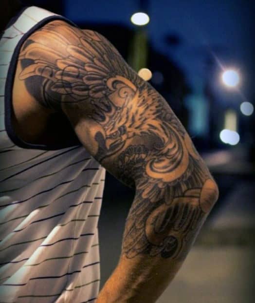 Arm with intricate eagle tattoo, wearing a striped tank top, evening background