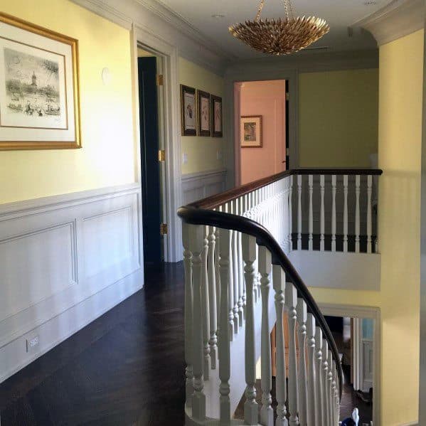 Charming hallway with white chair rail molding, yellow walls, dark wood flooring, and a vintage chandelier for a classic look