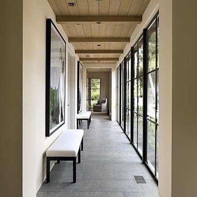 Modern hallway with wood beam ceiling, large windows, framed artwork, and white benches.