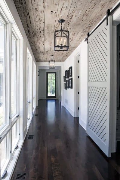 Rustic hallway with distressed wood ceiling, dark floors, sliding barn door, and lantern lights.