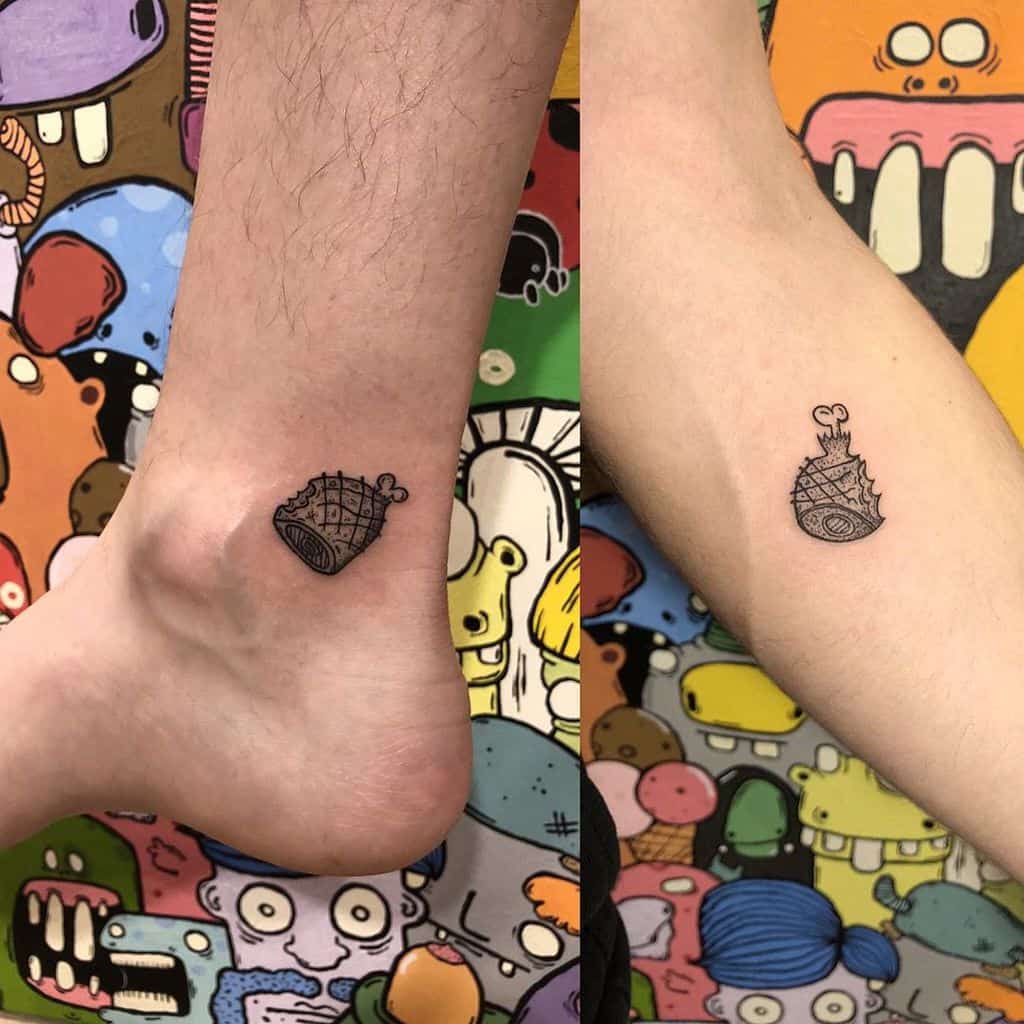 Matching small tattoos of a ham with a bone, designed to resemble a hand grenade, placed on the ankles in a quirky and humorous style.