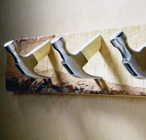Three hammers embedded in a wooden plank mounted on a wall