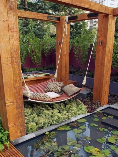 Backyard with wooden pergola, cozy hammock, lily pond, and lush green surroundings.