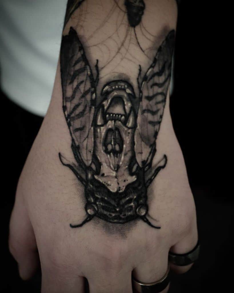 Black and white tattoo of a cicada on a hand, with detailed wings and head