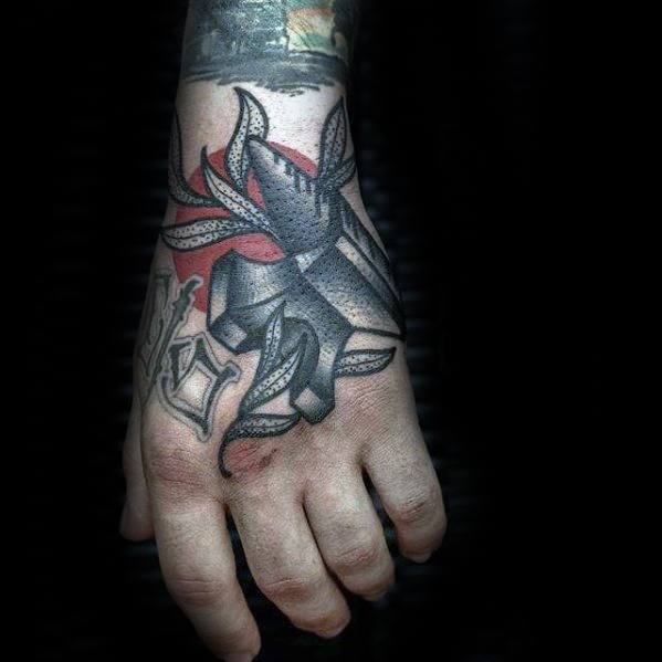Hand tattoo featuring a shaded black anvil wrapped in leaves, with red background highlights and bold lettering on the fingers.