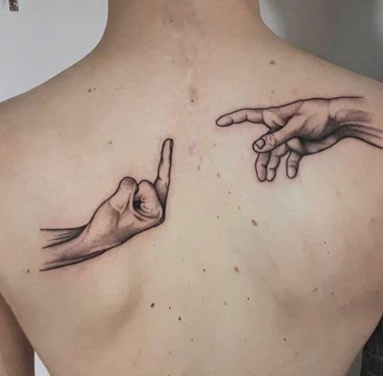 A humorous back tattoo parodying Michelangelo's 'The Creation of Adam,' with one hand flipping the middle finger instead of reaching out.