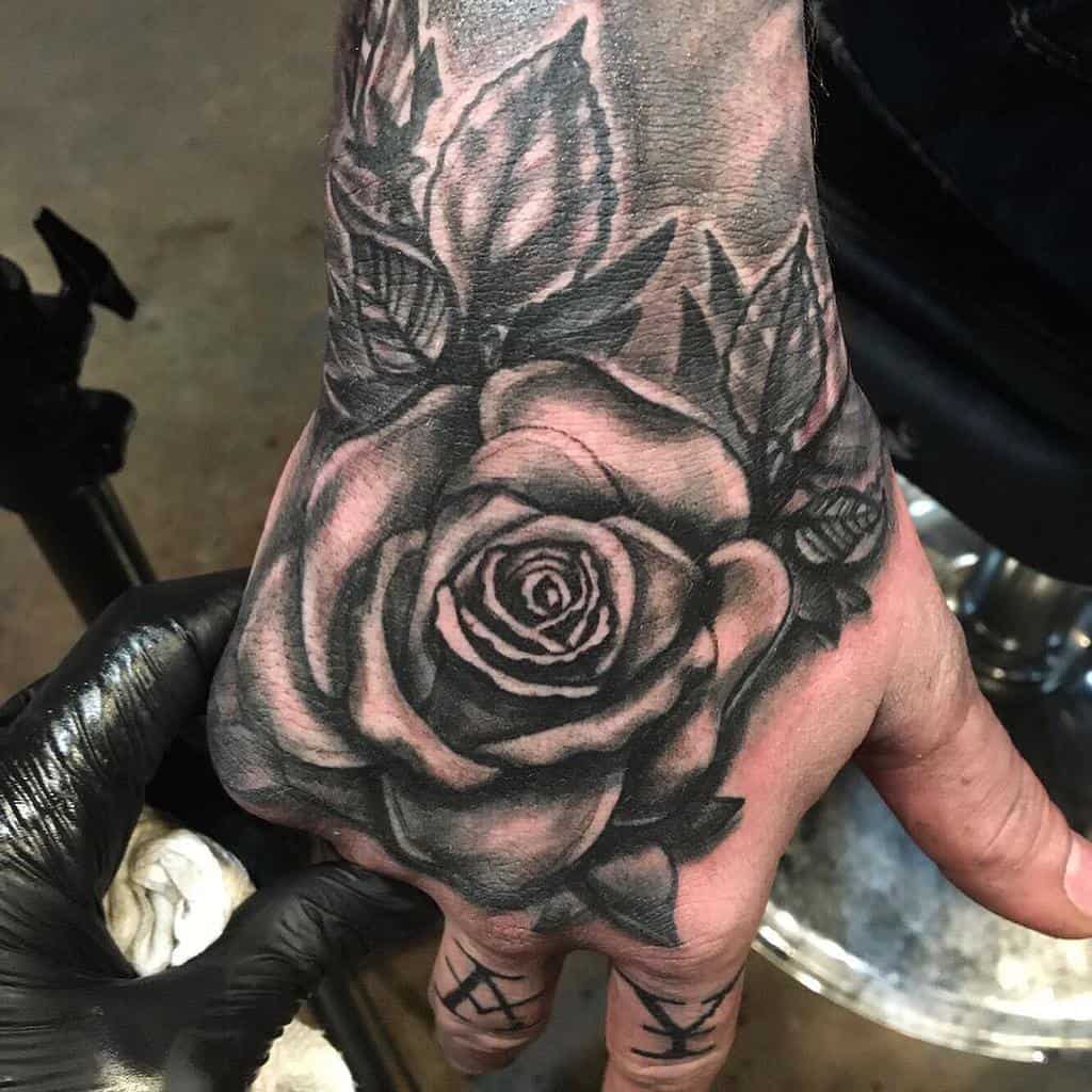 A black and gray rose tattoo on the back of a hand near the wrist