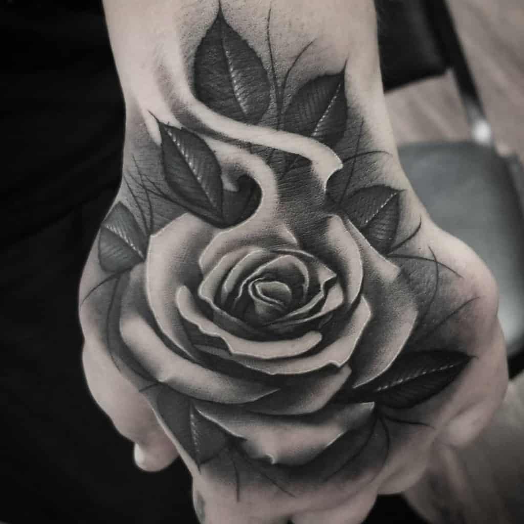 Black and gray rose tattoo on a hand with detailed shading and leaves