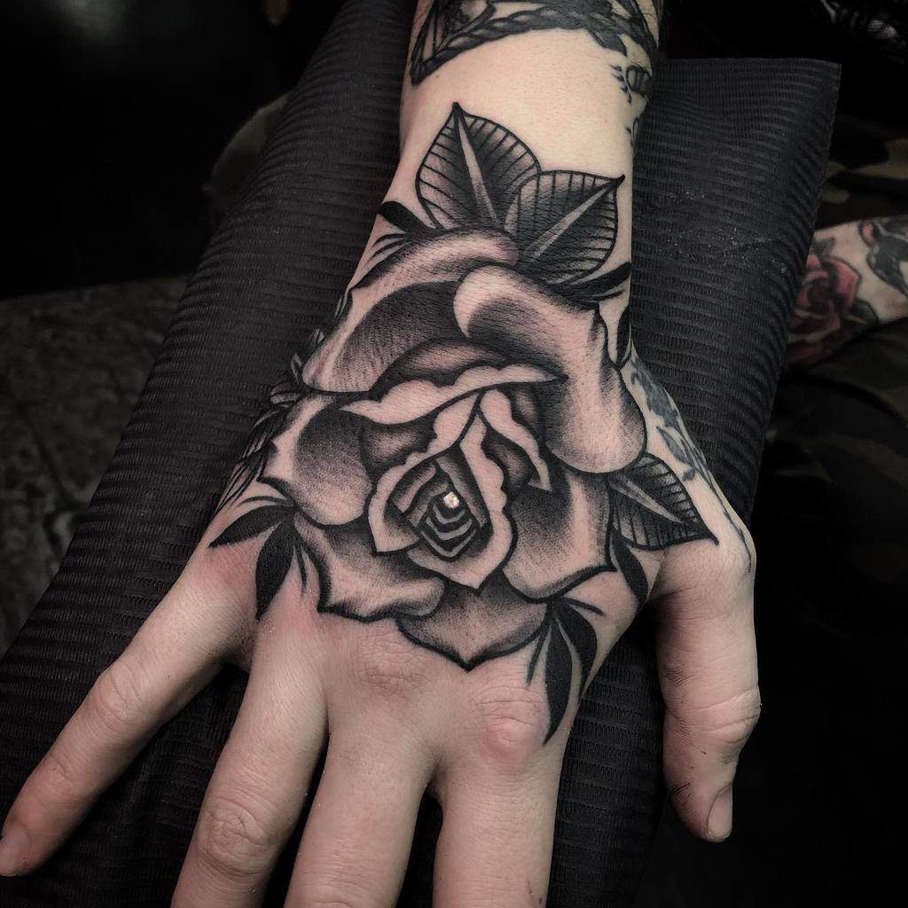 Hand with detailed black and white rose tattoo featuring leaves and shading on the back