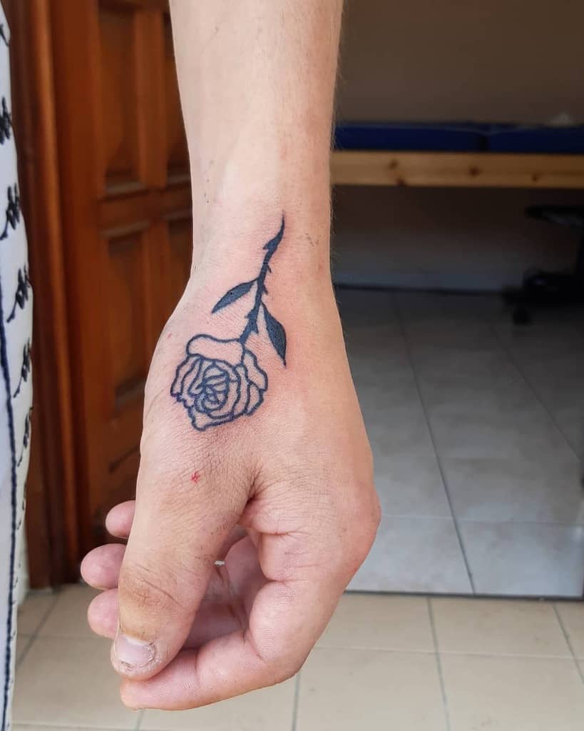 A forearm tattoo featuring a delicate rose intertwines elegantly down to the hand, with its stem and leaves adding an intricate touch