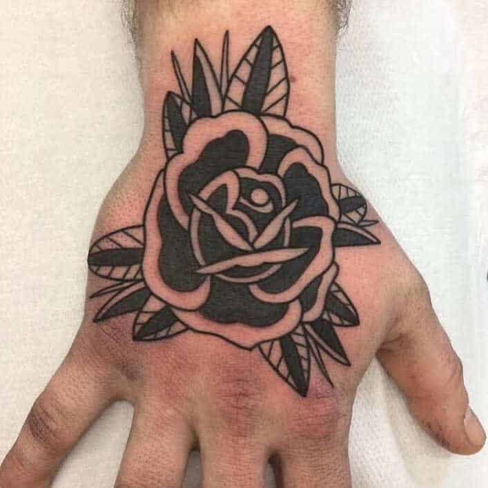 Tattoo of a bold, black rose with leaves on the back of a hand