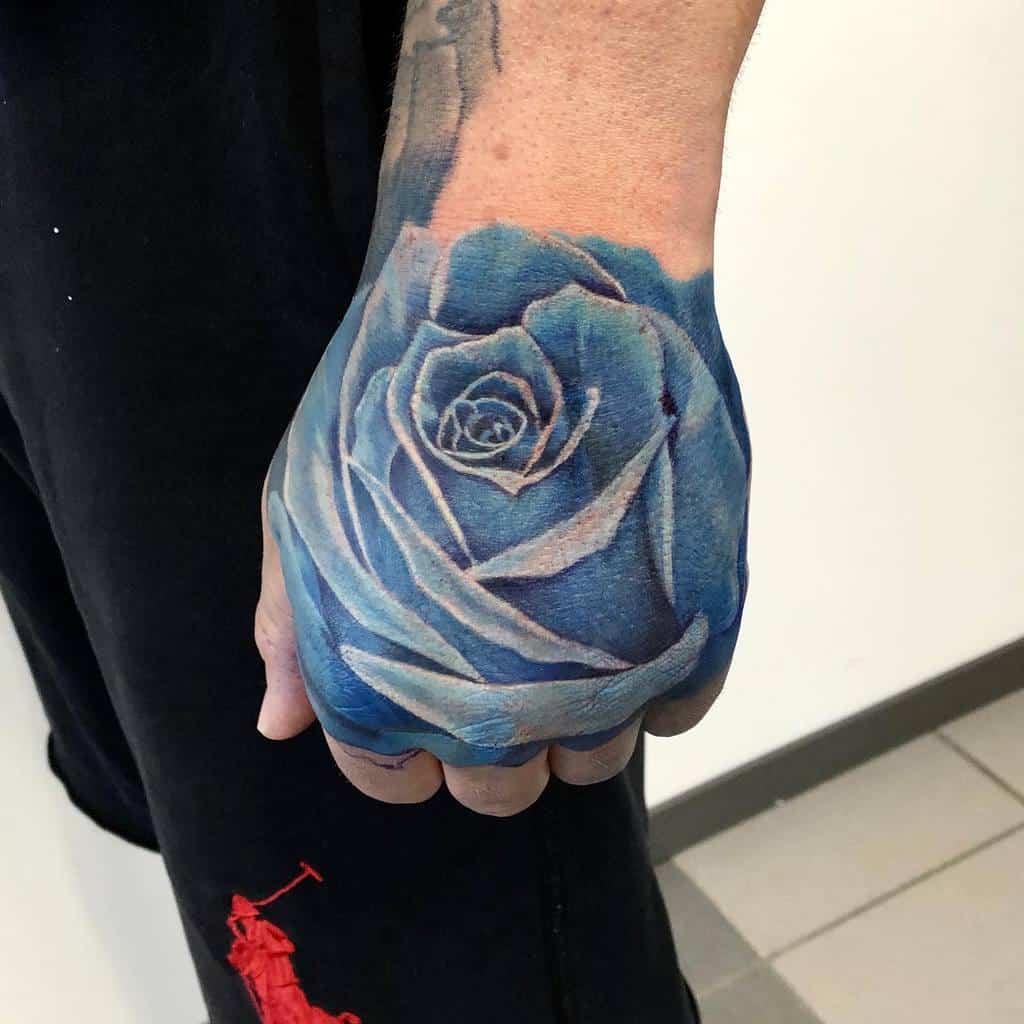 A realistic blue rose tattoo covering the hand and part of the forearm, showcasing detailed shading and highlighting to create depth and texture